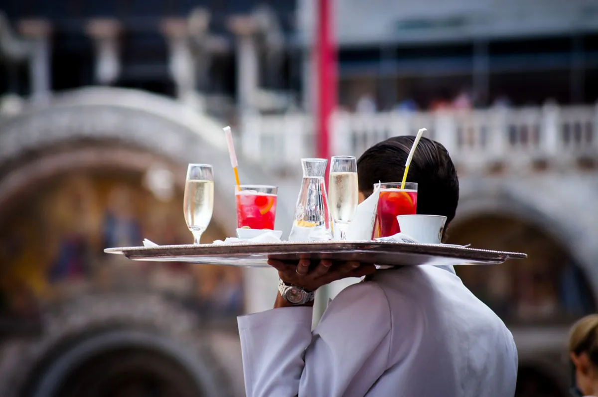 A server carrying a tray of drinks past an outdoor restaurant patio