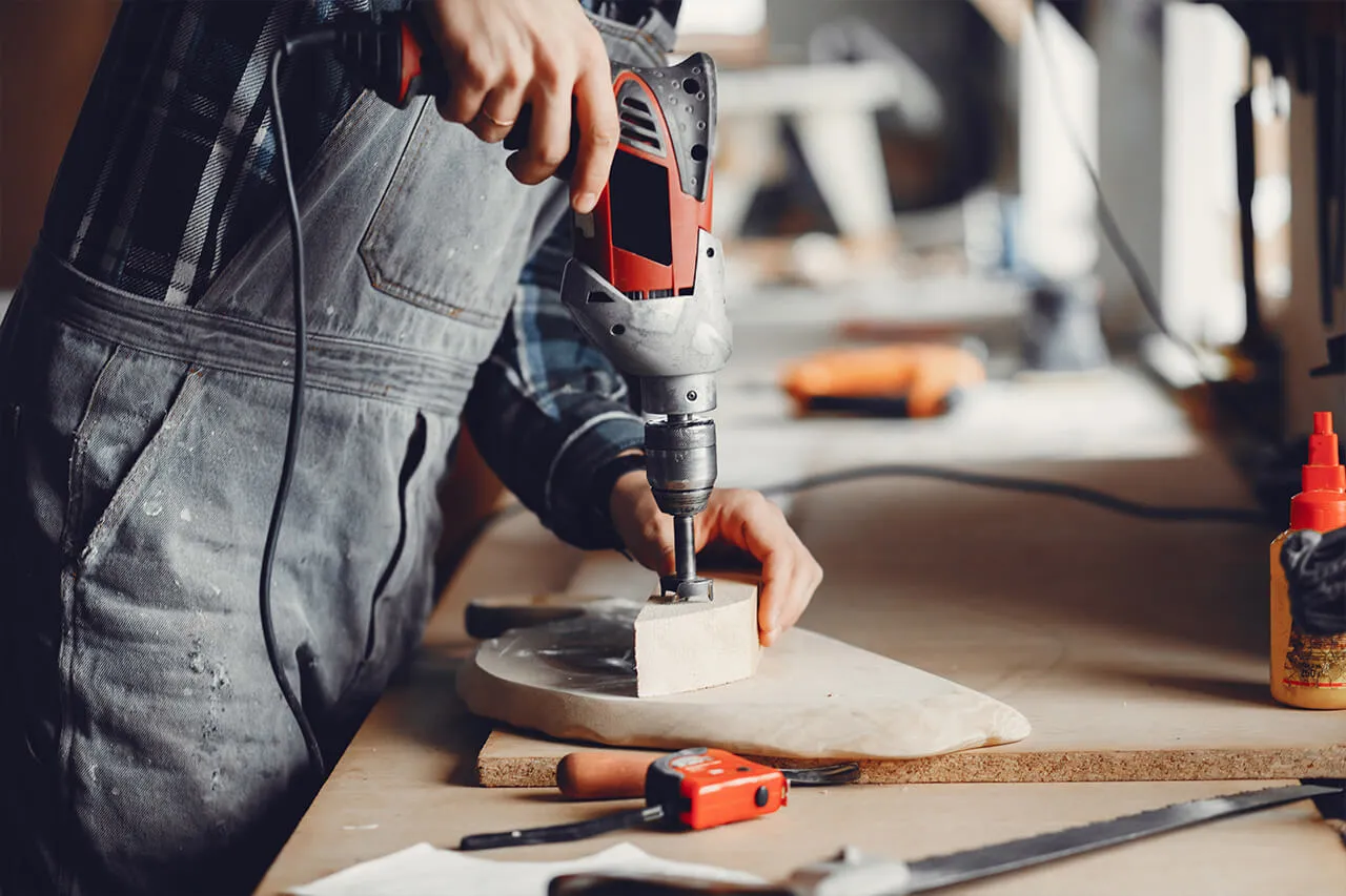 A worker in overalls using a power drill on a workbench