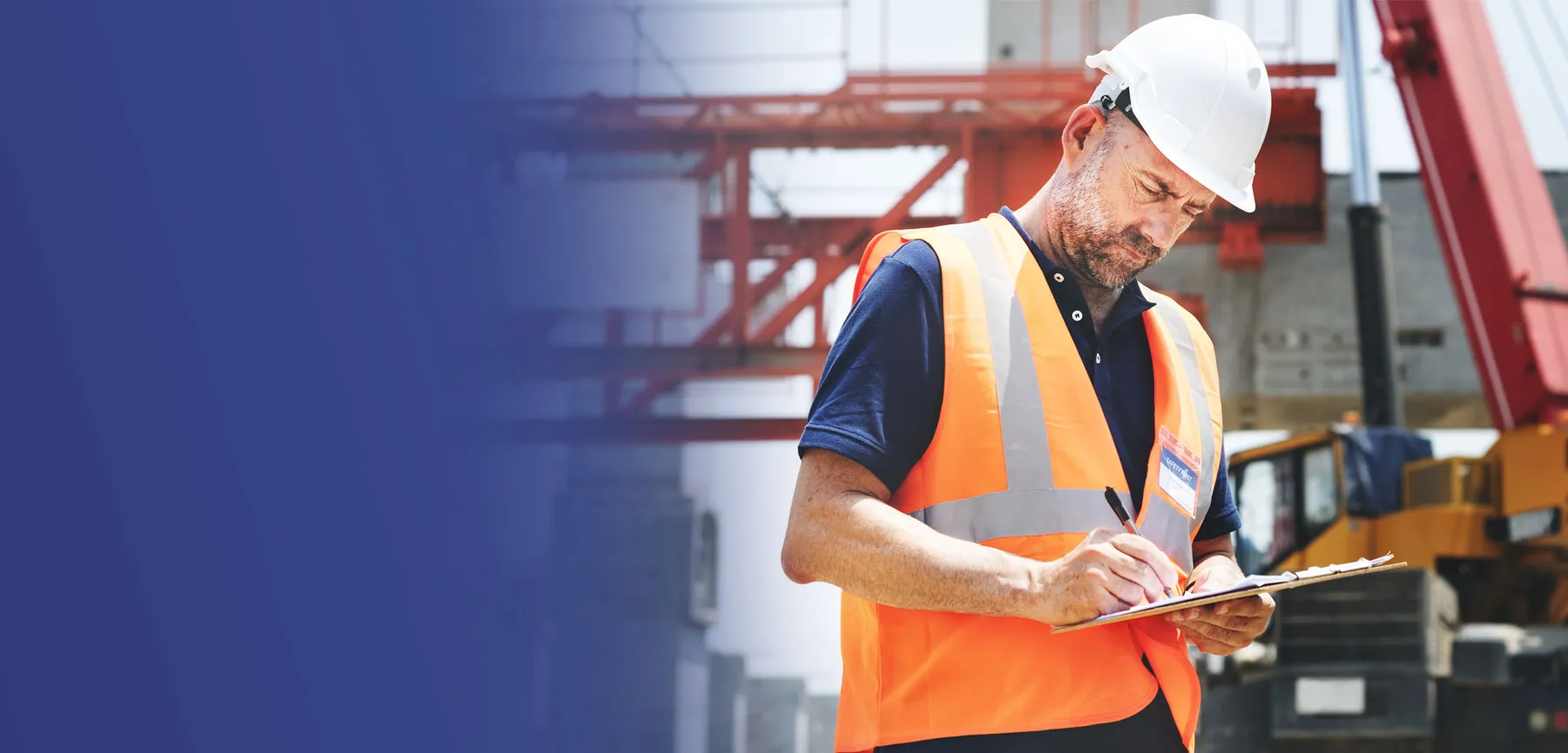 A construction supervisor in a hard hat and safety vest reviews paperwork on a clipboard at a job site