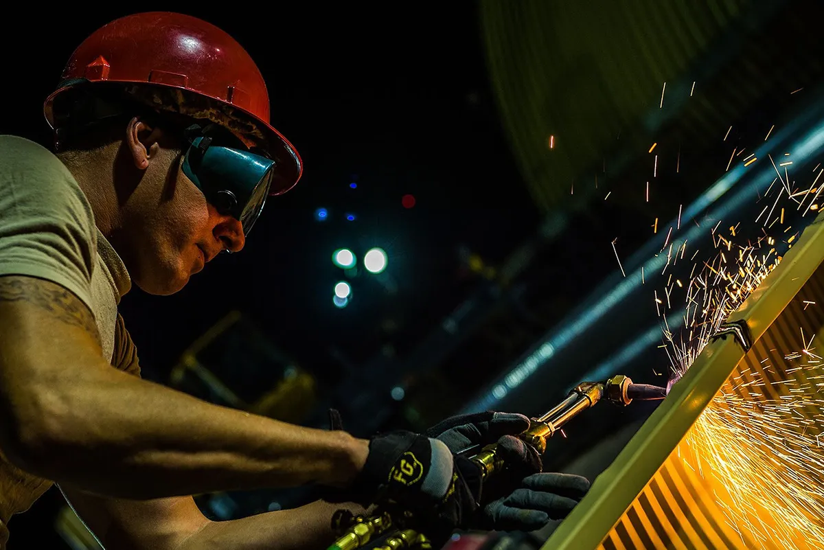 A construction worker welding metal at sunset, sparks flying